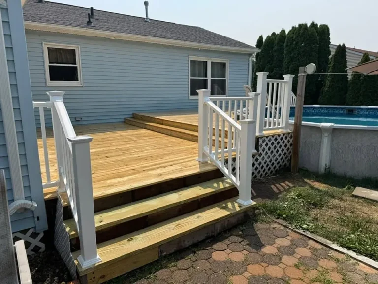 Deck with stairs and white railings next to an above-ground pool