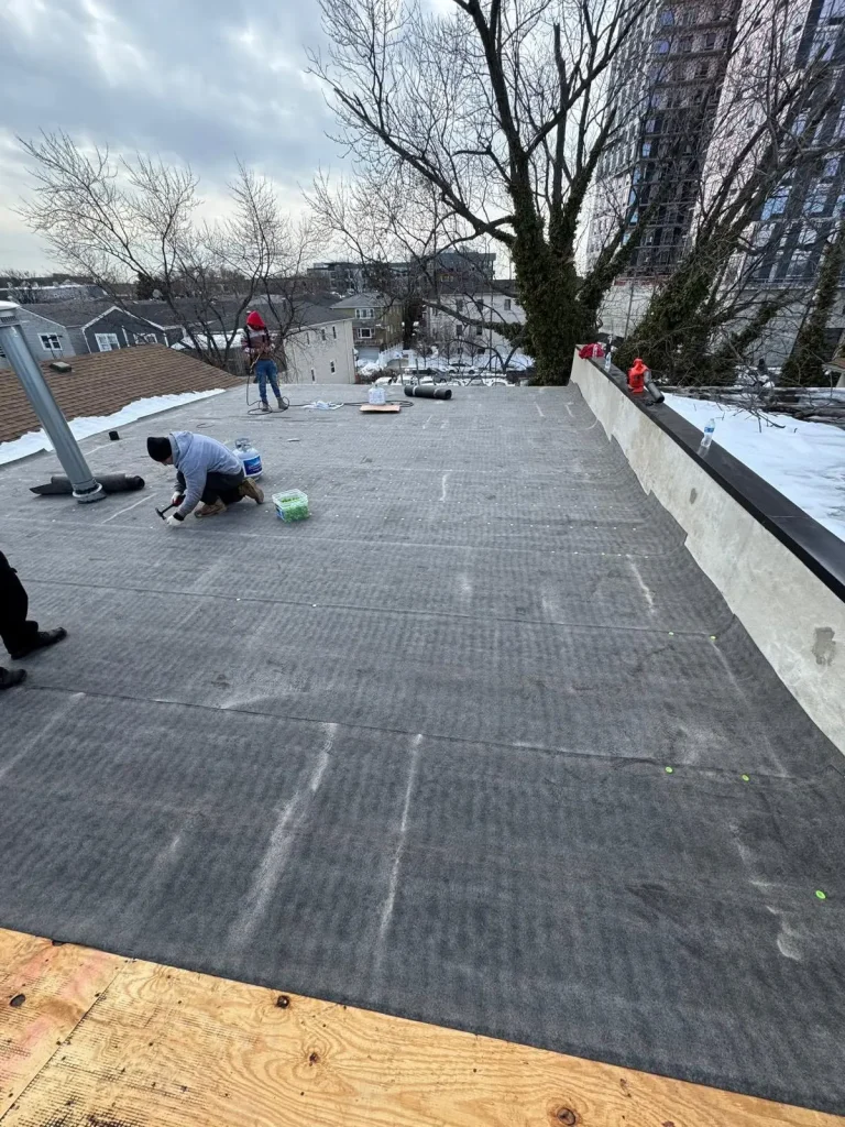 Crew installing a new flat roof membrane on a city row house