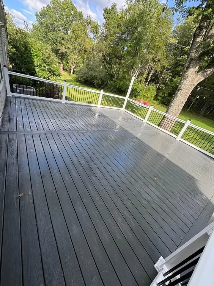 Large gray composite deck with white railings in a wooded backyard