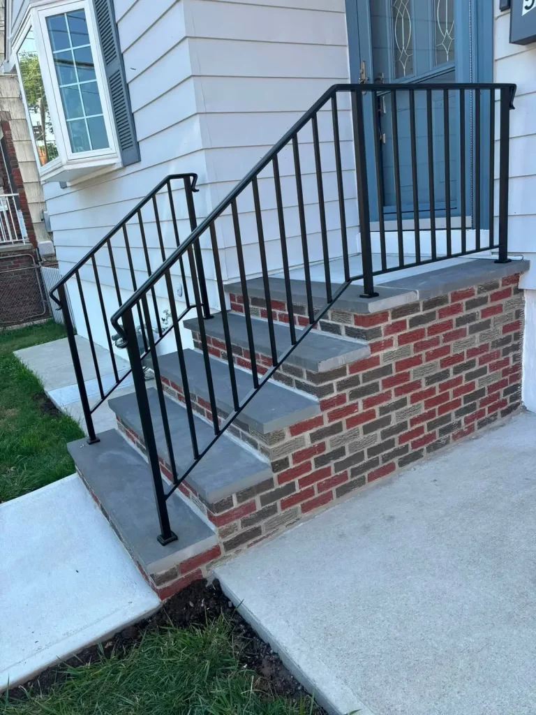 New brick stoop with black metal railings and a poured concrete walk