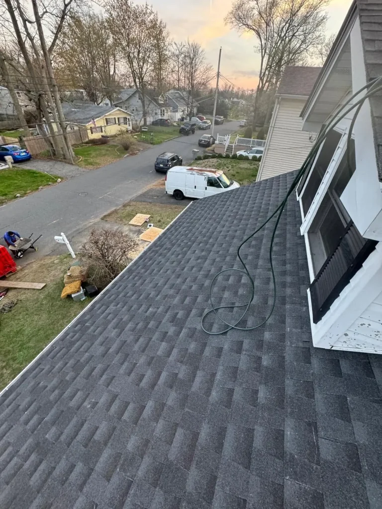 New charcoal architectural shingle roof seen from above, with the street and work trucks below