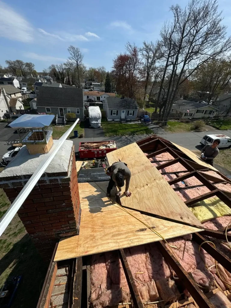 Roofer working beside a brick chimney during a re-roof, with new plywood decking